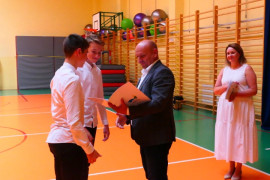 Chłopcy z rąk mężczyzny odbierają dyplom. Tuż za nimi stoi kobieta