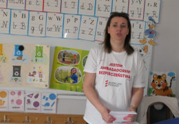 Kobieta stoi przy biurku i prowadzi spotkanie z dziećmi  