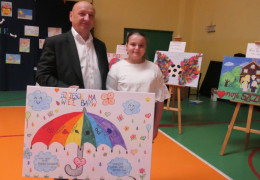 Mężczyzna oraz dziewczynka stoją obok siebie. Oboje trzymają pracę konkursowa, na której znajduje się kolorowy parasol 