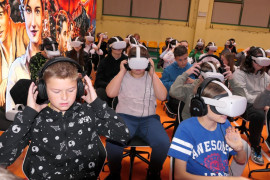 Młodzież szkolna - uczniowie siedzą na krzesłach, część z nich na słuchawki na uszach, większość na założone okulary VR
