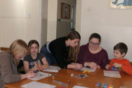 Uczestnicy warsztatów plastycznych. Osoby siedzą przy stole i robią ozdoby
