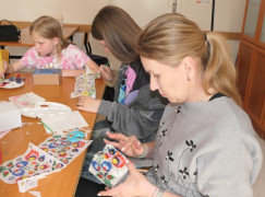 Dorośli i dzieci uczestniczą w warsztatach decoupage. Trwa robienie ozdobnych pudełek 