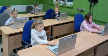 Uczniowie siedzą w szkolnych ławkach. Uczniowie korzystają z laptopów 
