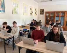 Uczniowie siedzą w szkolnych ławkach. Uczniowie korzystają z laptopów 