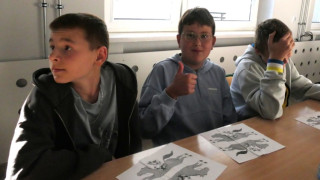 Trzej chłopcy siedzą w szkolnej ławce. Uczestnicy warsztatów