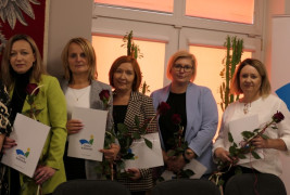 Pięć kobiet stojących na tle okna. Panie trzymają w ręku czerwone róże 