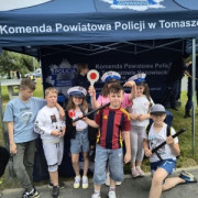 Dzieci stoją obok siebie. Za nimi znajduje się policyjny namiot 
