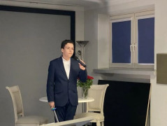 Chłopiec w garniturze trzyma w ręku mikrofon. Chłopiec recytuje wiersz