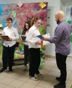 Dwie dziewczynki i chłopiec stoją obok siebie. Mężczyzna wręcza im dyplomy 