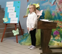 Dziewczynka podczas recytacji wiersza. Dziewczynka stoi obok stolika 