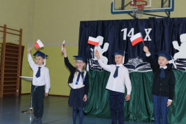 Uczniowie w galowych strojach trzymają w rączkach biało - czerwone flagi 