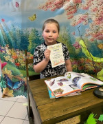 Dziewczynka siedzi za stolikiem. W ręku trzyma dyplom 