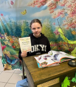 Dziewczynka siedzi za stolikiem. W ręku trzyma dyplom 