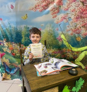 Chłopiec siedzi za stolikiem w ręku trzyma dyplom 