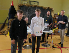 Dwaj chłopcy stoją obok siebie. Jeden z nich trzyma w ręku dyplom 