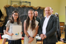 Dwie nastolatki stoją obok mężczyzny. Jedna z nich trzyma w ręku dyplom 