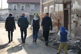 Grupa osób przechodzi obok zalanego domu